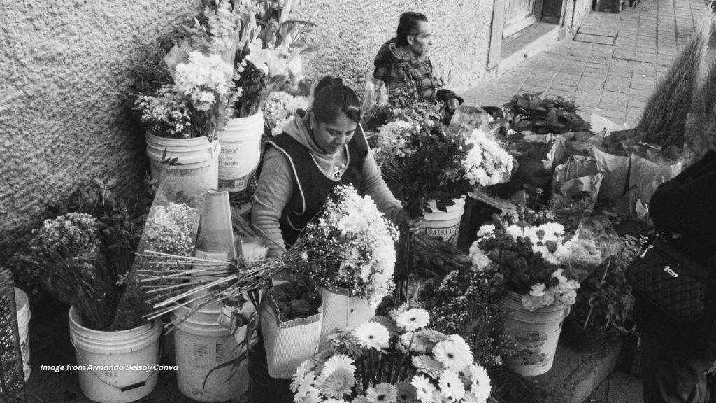 A flower vendor arranging blooms at an outdoor market stall, representing the humble origins behind every floral company story.